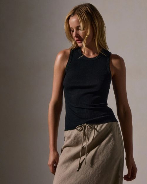 A woman wearing a fitted black tank top and a tan skirt, showcasing a stylish and casual outfit.