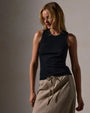 A woman wearing a fitted black tank top and a tan skirt, showcasing a stylish and casual outfit.