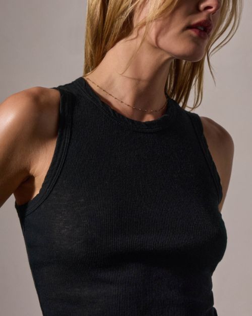 Model wearing a fitted black tank top made of soft, lightweight cotton cashmere rib with raw hem and jersey binding details.