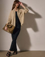 A woman in a black dress holds a brown bag, complemented by a wool blend button-up shirt.