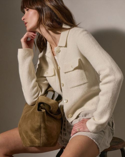 A woman wearing an ivory knit sweater and shorts sits on a stool, exuding a relaxed and casual vibe.