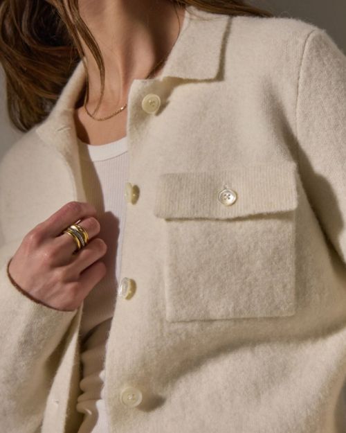 The model wears an ivory sweater knit jacket paired with a gold ring, exuding elegance.