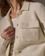 The model wears an ivory sweater knit jacket paired with a gold ring, exuding elegance.