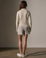 Back view of a woman wearing a stylish ivory sweater knit jacket and shorts, highlighting a casual look.