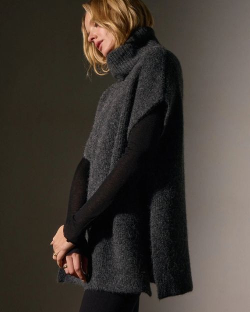 A woman in a waffle knit funnel neck tunic and black pants stands confidently, showcasing her stylish outfit.