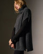 A woman in a waffle knit funnel neck tunic and black pants stands confidently, showcasing her stylish outfit.