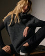 A woman wearing a waffle knit funnel neck tunic and sneakers sits confidently.
