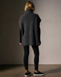  Woman's back view wearing a waffle knit funnel neck tunic paired with black leggings, highlighting a relaxed style.