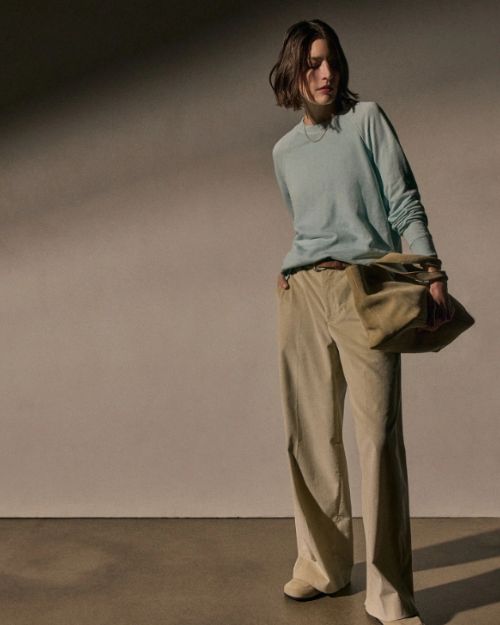 A woman wearing a fresco-colored boyfriend raglan sweatshirt and wide pants, standing confidently against a neutral background.