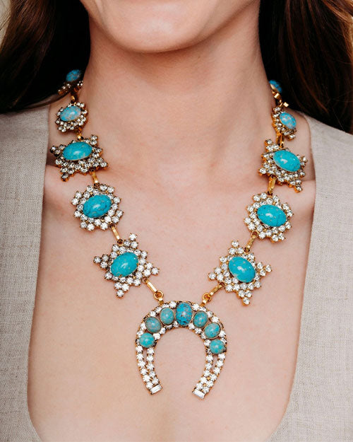 A woman adorned with a traditional Squash Blossom necklace, showcasing a turquoise matrix stone and sparkling crystals.