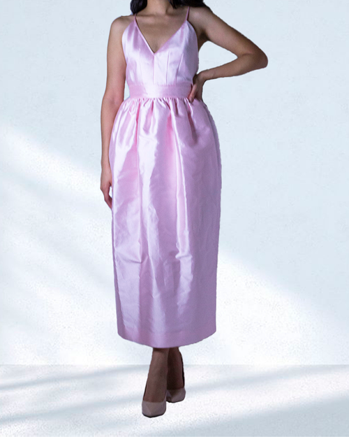 Brunette model wearing pink silky dress in front of white background.
