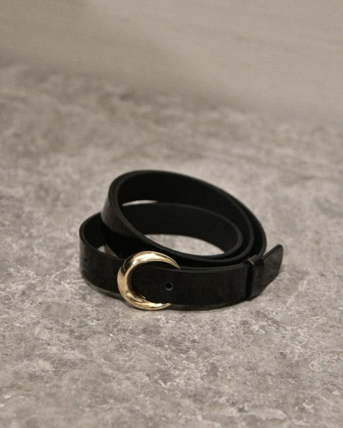 Black leather belt with gold buckle placed on marbled cement surface.