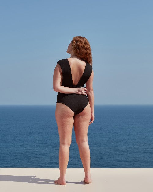 Model turned away from camera to show V-Back of swimsuit.