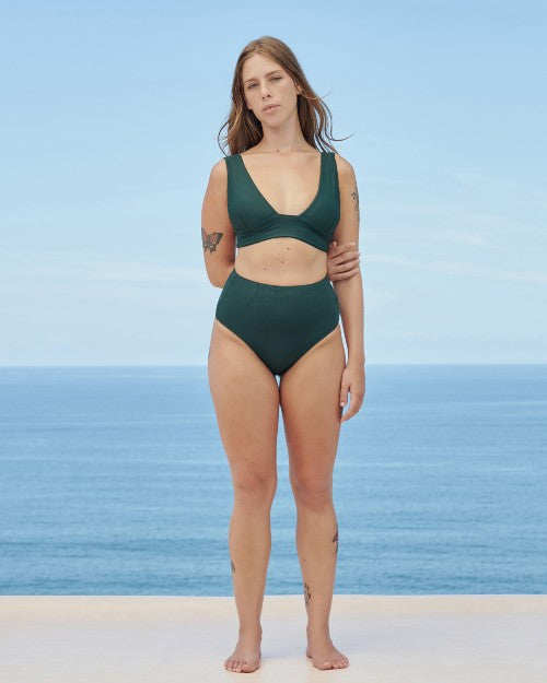 Model wearing Vintage Swimsuit Bottom in pine green in front of beach/ocean backdrop. 