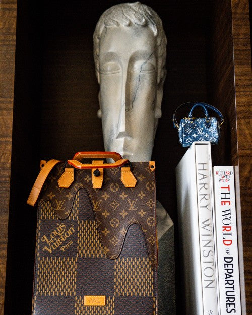Bijoux Sack Micro Speedy Bag Charm on top of book spine on bookshelf.