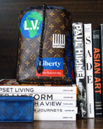 Louis Vuitton Chalk Sling Bag on top of books on bookshelf.