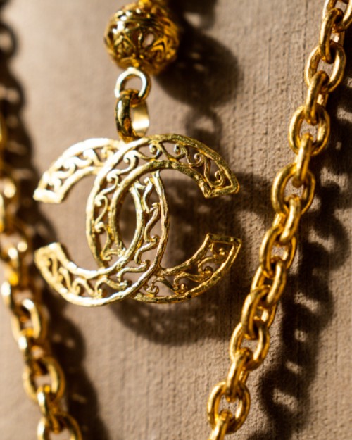Gold Chanel logo necklace in front of tan canvas material.