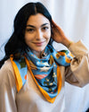 Model wearing 12 Days of Christmas Silk Cream Scarf around neck while smiling at camera.
