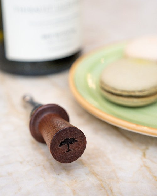 The Post Oak Rosewood Wine Stopper on light brown marble table.