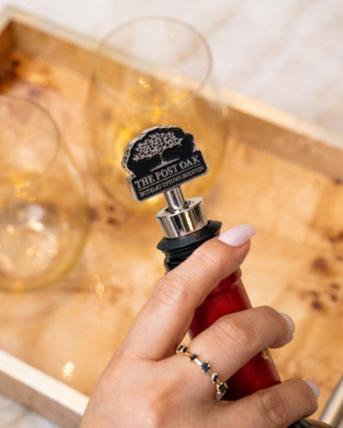 Woman holding wine bottle that has The Post Oak wine stopper at the top. 