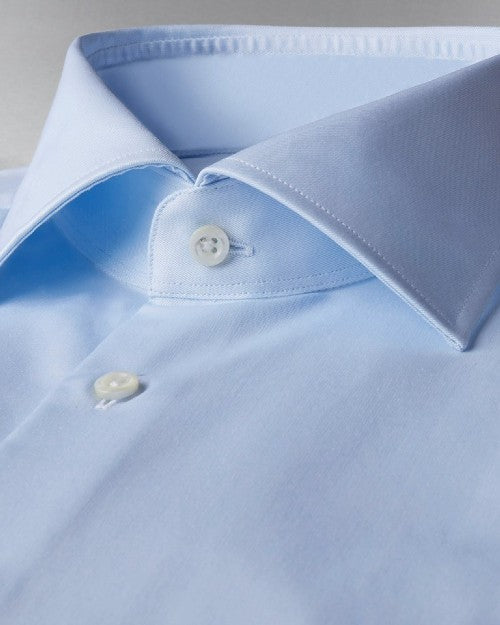 A zoomed in view of a light-blue button-down shirt with clear buttons. The background is grey.