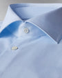 A zoomed in view of a light-blue button-down shirt with clear buttons. The background is grey.