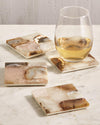 Brown/cream marble coasters on white marble table with stemless wine glass.