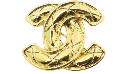 Gold Chanel logo brooch in front of white background.