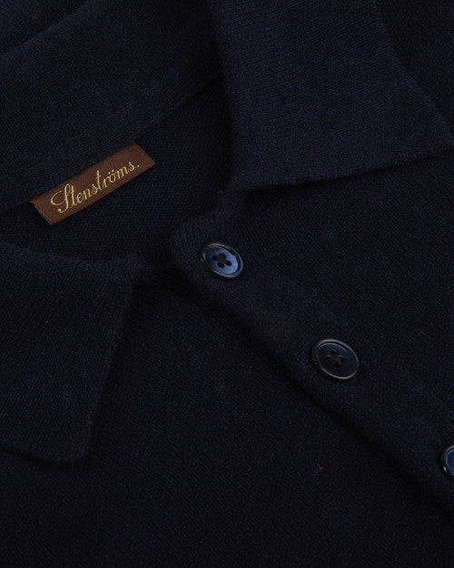A close-up image of three navy buttons on a navy collared polo-shirt, with a rectangular brown tag and the word "STENSTRӦMS" printed on it.