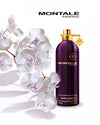 Montale Dark Purple pefume bottle next to white orchids in front of white background. 