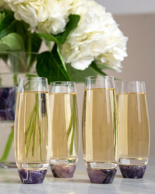 Elevo Champagne Glasses with amethyst bottoms in front of white floral arrangement.