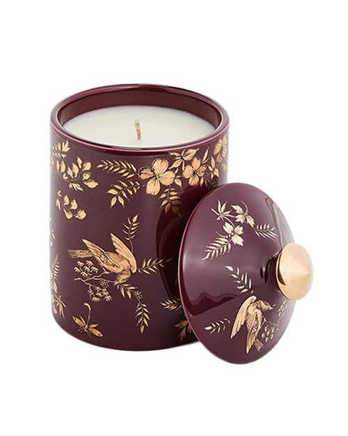 White candle in red jar and lid with gold floral and bird design.