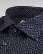 A zoomed in view of a navy button-down shirt featuring an intricate arrowlike triangular pattern and black buttons. The background is grey.
