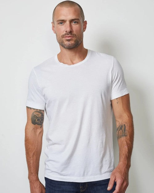 Model wearing Howard Men's Tee in white with blue jeans in front of white background. 