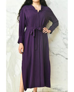 Model wearing purple long dress with long sleeves in front of a white marble background.