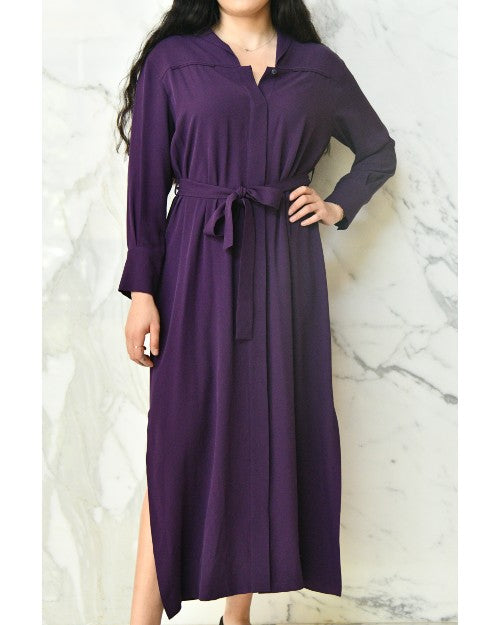 Model wearing purple long dress with long sleeves in front of a white marble background.