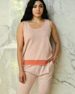 Model wearing rose pink top with bottom coral stripe and matching rose pink pants in front of marble wall. 