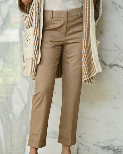 Model wearing tan trousers with white tee and brown cardigan in front of marble background.