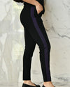 Side view of model wearing Black Purple Knit Trousers in front of white marble wall, showing purple stripe.