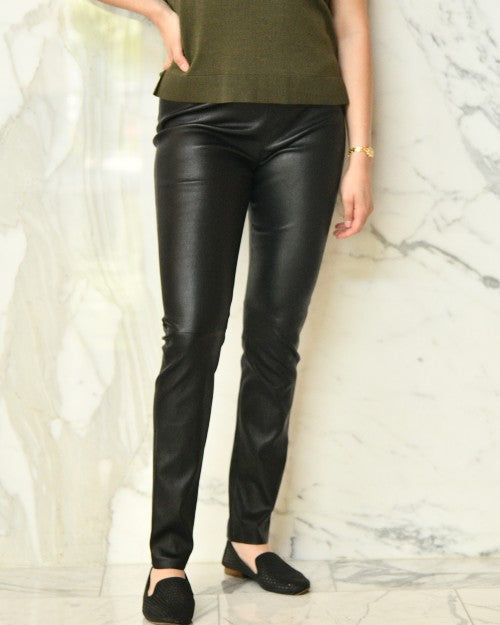 Model wearing black leather leggings in front of marble background.