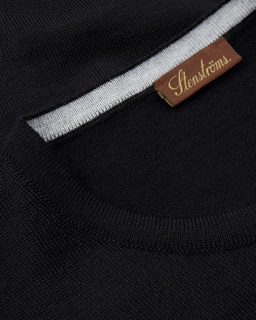 A close-up view of a folded black shirt's crewneck neckline with a white stripe inside, and a rectangular brown tag reading "STENSTRӦMS". 