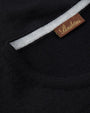 A close-up view of a folded black shirt's crewneck neckline with a white stripe inside, and a rectangular brown tag reading "STENSTRӦMS". 