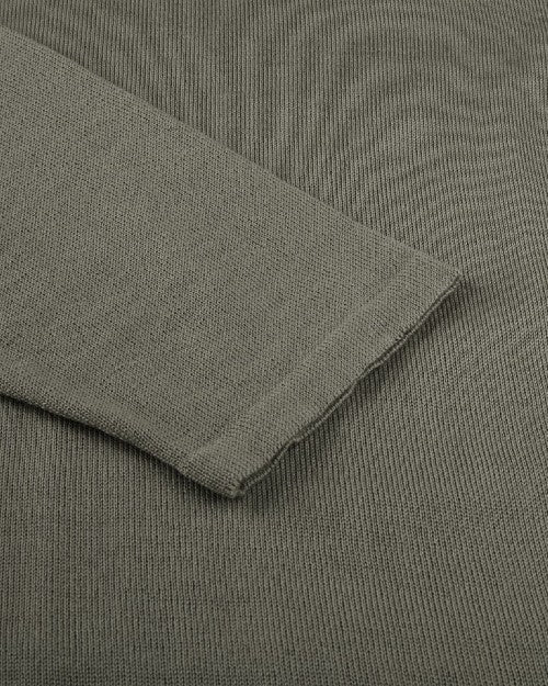 A close-up view of a long-sleeve shirts wrist cuff placed on the green shirt fabric. 