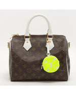 Dark brown Louis Vuitton bag with iconic pattern, white handle, and tennis ball coin purse keychain.