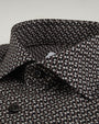 A zoomed in view of a button-down shirt featuring a small, intricate geometric pattern and black buttons. The background is grey.