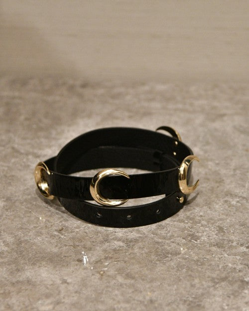 Black leather belt with gold moon buckles in front of marbled cement surface. 